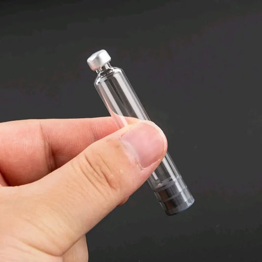 A hand holds an empty, clear 3ml glass vial with a silver cap.