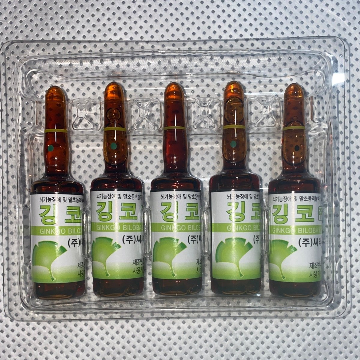 Five amber ampules of Ginkgo Biloba extract are arranged in a clear plastic tray.