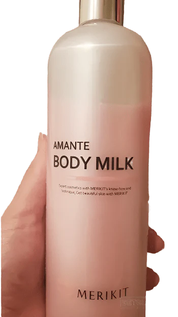 A hand holds a pink bottle of MERIKIT Amante Body Milk.