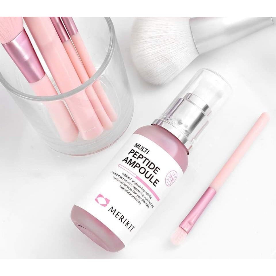 A pink Merikit Multi Peptide Ampoule Serum bottle is on a white surface with makeup brushes.