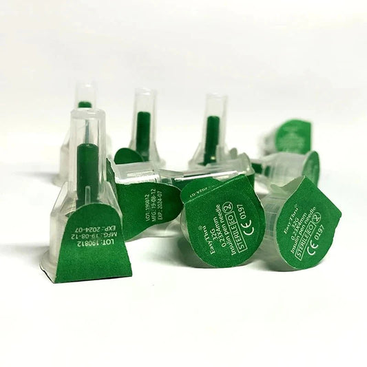 Several green-capped insulin pen needles are scattered on a white surface.