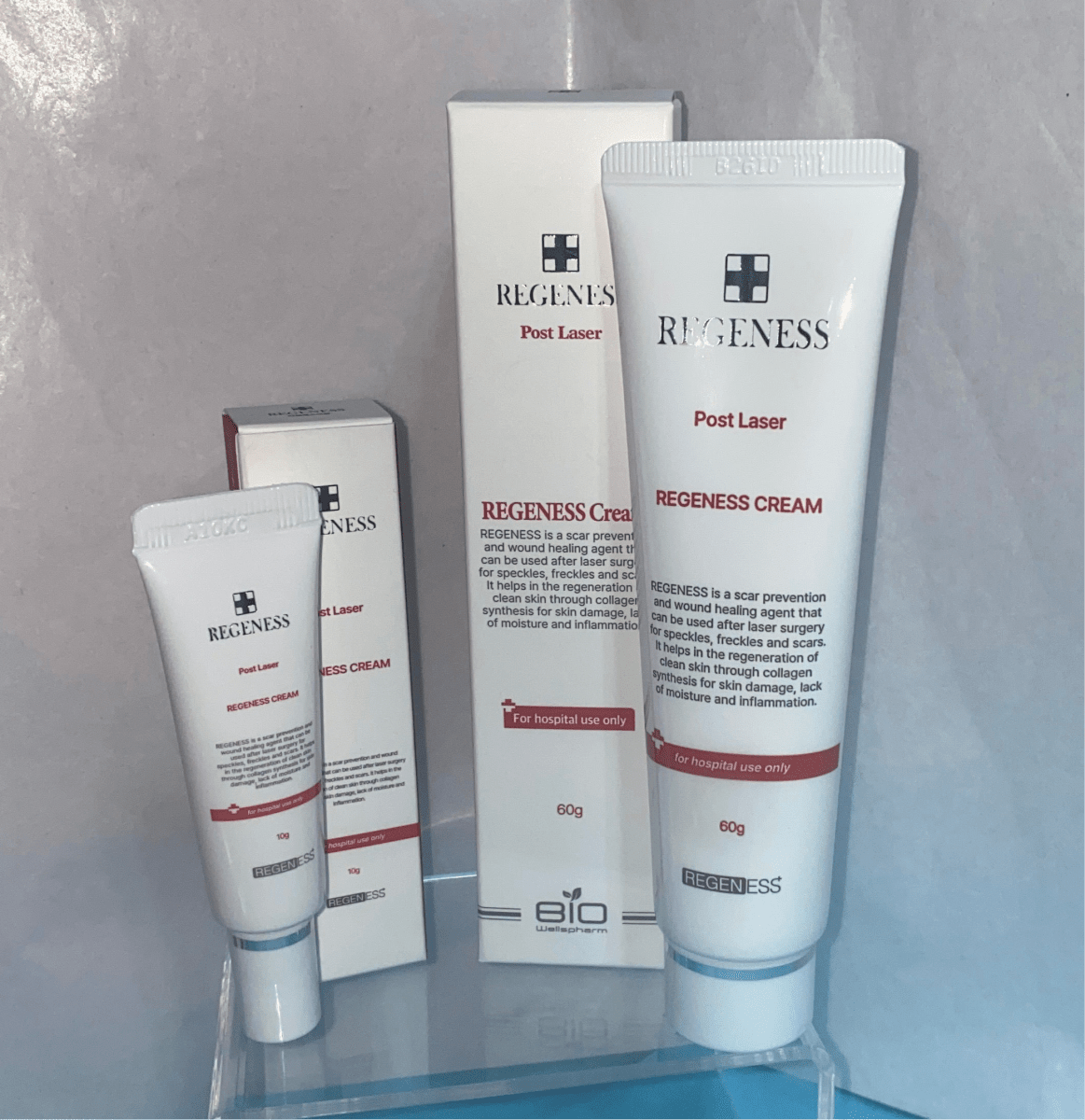Three white tubes and two boxes of Regeness Post Laser cream are displayed on a clear stand.